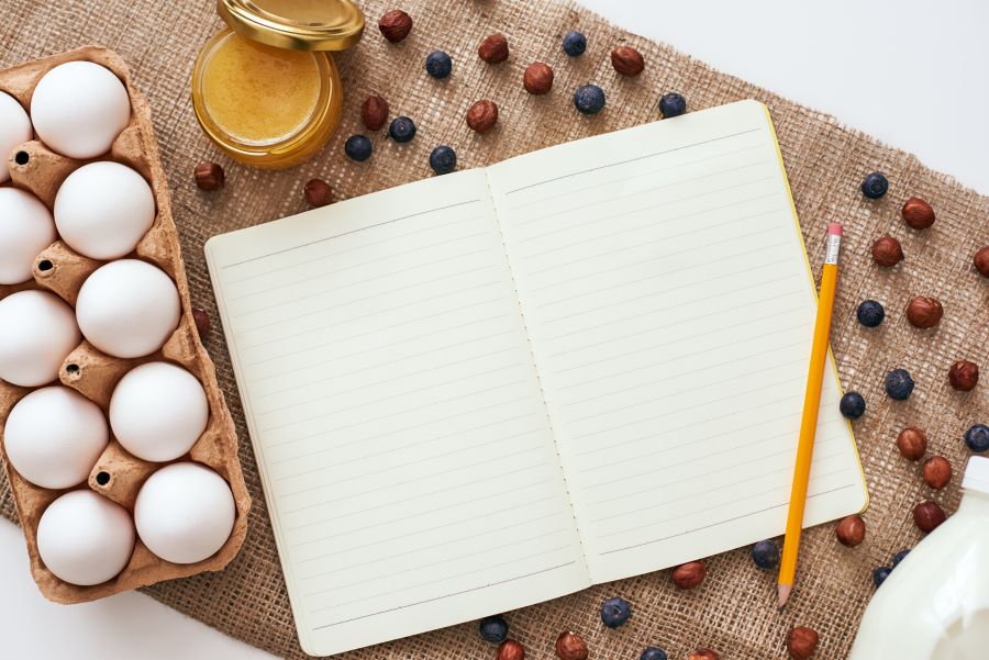 Eier, Beeren und Honig auf einem Tisch mit einem Notizbuch und Stift in der Mitte